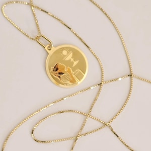 May include: A gold chain necklace with a round pendant featuring a religious image of a person praying with a chalice and sun above.