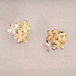 May include: A pair of gold, silver, and rose gold flower-shaped earrings. The earrings are made of three flowers each, with the flowers overlapping each other.