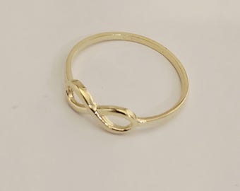 May include: A gold-colored ring featuring an infinity symbol design. The ring is a simple band with the infinity symbol as the focal point. The ring is likely made of gold or a gold-toned metal.