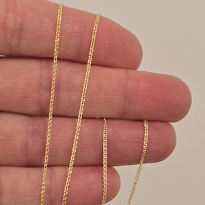 May include: A thin, delicate gold chain necklace featuring a fine, interlocking link design. The metallic yellow gold material has a reflective, polished finish that catches the light, creating a subtle shimmer along the length of the slender chain.
