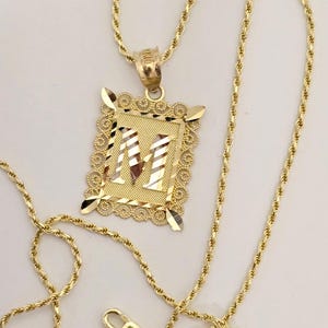 May include: A gold chain necklace with a pendant featuring the letter "M" in a decorative frame.