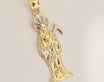 May include: A two-tone gold pendant featuring a figure draped in a long robe holding a scythe. The figure has a circular halo behind the head. The pendant includes a bail at the top for attachment to a chain, crafted with yellow and white gold.