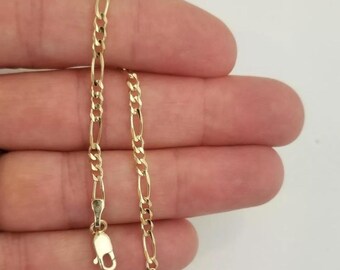 May include: A gold chain bracelet with a figaro link pattern. The bracelet is approximately 7 inches long and has a lobster claw clasp.
