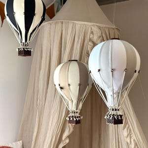 Puede incluir: Tres globos aerostáticos colgando del techo. Los globos están hechos de tela y tienen un patrón a rayas. Los globos son blanco y negro, blanco y gris, y beige y marrón. Los globos están colgando de un dosel blanco.