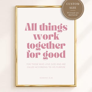 Op de afbeelding: Een ingelijste kunstprint met de roze tekst "All things work together for good" gevolgd door "FOR THOSE WHO LOVE GOD AND ARE CALLED ACCORDING TO HIS PURPOSE" en "ROMANS 8:28". Een ronde bruine badge in de hoek vermeldt "CUSTOM SIZE Printed on demand".