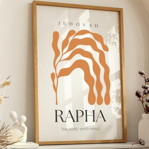 Puede incluir: Impresión artística enmarcada en madera con las palabras "JEHOVAH" y "RAPHA" en fuente negra. La impresión presenta un diseño abstracto naranja y el texto "THE LORD WHO HEALS". La obra de arte se exhibe en un mueble blanco.
