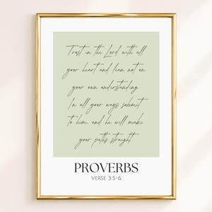 Op de afbeelding: Een ingelijste wandkunstprint met een saliegroene achtergrond en zwarte cursieve tekst: Trust in the Lord with all your heart and lean not on your own understanding. In all your ways submit to him, and he will make your paths straight. Daaronder staat de tekst: PROVERBS VERSE 3:5-6. De print is gevat in een dunne, goudkleurige metalen lijst.