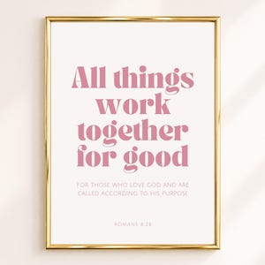 Op de afbeelding: Een ingelijste wandkunstprint met de tekst All things work together for good in een vet roze schreeflettertype, gevolgd door de kleinere tekst FOR THOSE WHO LOVE GOD AND ARE CALLED ACCORDING TO HIS PURPOSE en ROMANS 8:28 in een gouden lijst.
