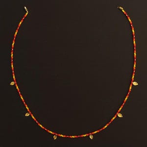 May include: A gold necklace with small red and yellow beads and gold leaf charms.