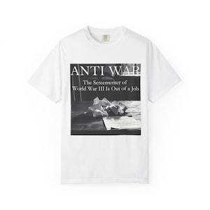 以下が含まれることがあります： 白のTシャツ。黒と白のグラフィックが特徴です。グラフィックには、「ANTI WAR」の文字と、くしゃくしゃになった紙とスクリプトの白黒画像が描かれています。画像の下のテキストは「The Screenwriter of World War III Is Out of a Job」と書かれています。