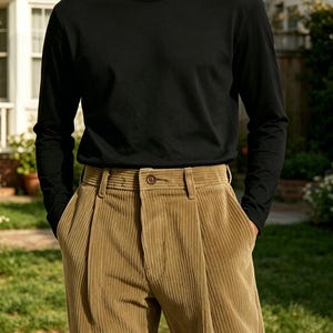 May include: A long-sleeved black crew neck shirt paired with tan corduroy trousers. The trousers feature a high-waisted design with a single brown button closure, belt loops, and prominent vertical pleats running down the front of each leg.