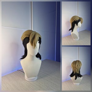 Könnte beinhalten: Perücke mit hellbraunem Oberteil und schwarzen Akzenten, auf einem Schaufensterkopf drapiert. Die Perücke hat ein mehrschichtiges Design mit Pony und längeren Strähnen am Hinterkopf. Die Schaufensterpuppe steht auf einem weißen Sockel vor neutralem Hintergrund.
