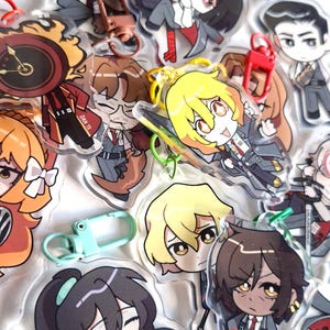 May include: A collection of clear acrylic keychains featuring various anime-style character designs. The keychains have colorful details, including red, yellow, and blue accents, and are attached to metal clasps. Some keychains have text.