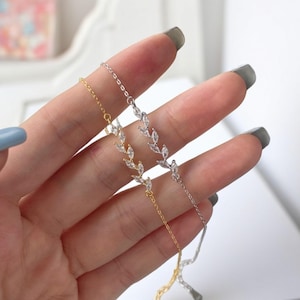 May include: Two delicate silver and gold chain bracelets with a leaf design featuring clear cubic zirconia stones.