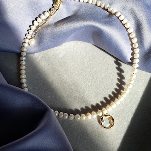 May include: A delicate pearl necklace with a gold pendant featuring a moon and stars design. The necklace is on a blue fabric background.
