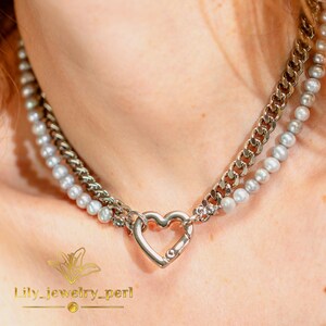May include: A silver-toned necklace featuring a heart-shaped clasp. The necklace combines a chain link design with a strand of small, round pearls. The text "Lily_jewelry_perl" is visible at the bottom.