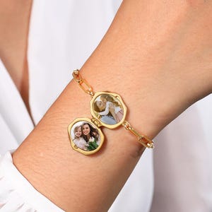 Puede incluir: Pulsera dorada con dos medallones ovalados, cada uno con una pequeña fotografía. La pulsera está unida con eslabones de cadena rectangulares dorados. Los medallones están abiertos, revelando las fotos.