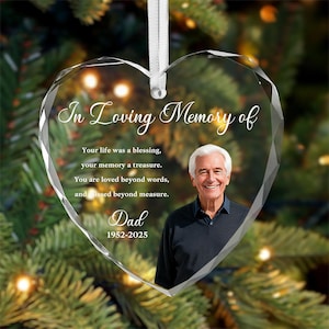 Può includere: Un ornamento di cristallo a forma di cuore con la scritta "In Loving Memory of" e la foto di un uomo. L'ornamento include il testo "Your life was a blessing, your memory a treasure. You are loved beyond words, and missed beyond measure. Dad 1952-2025."
