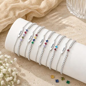 Peut inclure: Une collection de bracelets à chaîne argentée ornés de petites pierres précieuses carrées colorées et de plaques métalliques ovales gravées des noms Randal, Nannie, Fagan, Babbie et Ursula. Chaque bracelet présente un design à maillons fins.