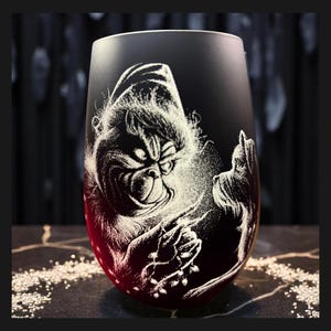Könnte beinhalten: Ein mattes, schwarzes, stieloses Weinglas mit einer weißen, lasergravierten Illustration eines mürrischen Charakters mit spitzem Hut und einem kleinen Hund. Das Design zeigt den Charakter, der eine Lichterkette in Punktiertechnik hält.