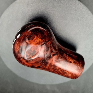 May include: A gear shift knob with a polished, dark reddish-brown burl wood grain finish. The top surface features white printed text showing the number 5 and the letter R, indicating a manual transmission gear pattern for a vehicle interior.
