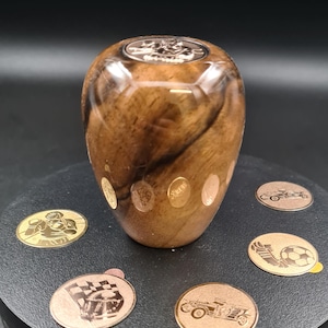 Può includere: Un pomello del cambio in legno con una venatura di legno marrone e nero. Il pomello ha una parte superiore in metallo dorato con un design ed è circondato da punti in metallo dorato.