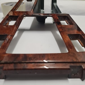 Puede incluir: Un embellecedor de consola central de coche con acabado brillante de veta de madera. El embellecedor es rectangular con varias aberturas y de color marrón oscuro. El patrón de veta de madera es visible.
