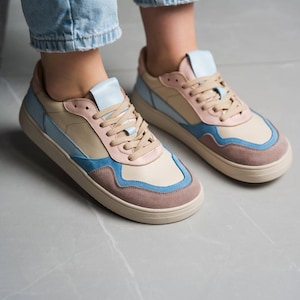May include: A pair of colorful sneakers with a beige base, accented with light blue, pink, and brown panels. The shoes have beige laces and soles. The sneakers are designed with a low-top profile.