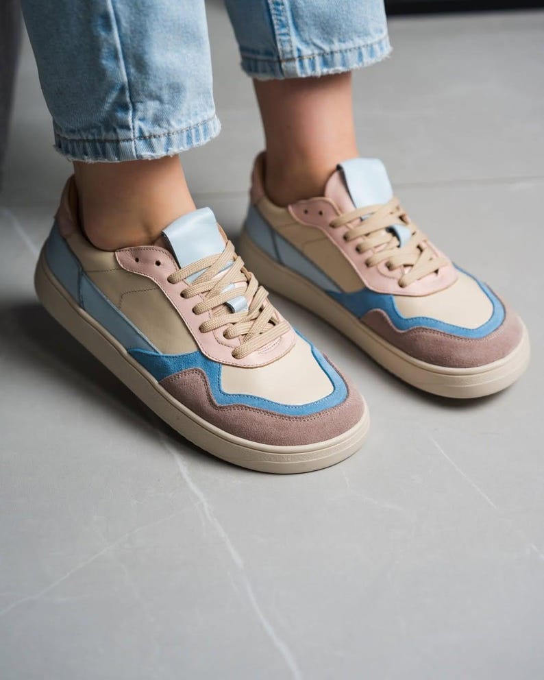 May include: A pair of colorful sneakers with a beige base, accented with light blue, pink, and brown panels. The shoes have beige laces and soles. The sneakers are designed with a low-top profile.