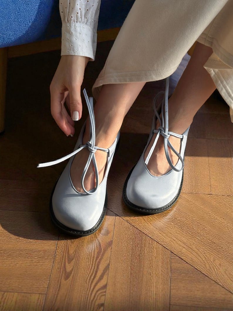 Op de afbeelding: Lichtblauwe Mary Jane-schoenen met een ronde neus en zwarte zolen. De schoenen hebben een bandje dat om de enkel wordt gestrikt. De schoenen zijn gemaakt van glad materiaal.