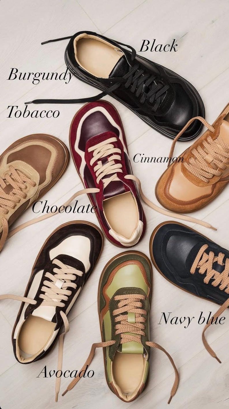 May include: A collection of seven pairs of sneakers in various colors, including black, burgundy, tobacco, chocolate, cinnamon, avocado, and navy blue. Each pair features matching laces and a neutral-colored interior.