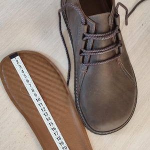 May include: A brown leather shoe with laces and a matching insole. The insole is measured with a ruler, showing a length of approximately 30 cm. The shoe has a rounded toe and a textured appearance.