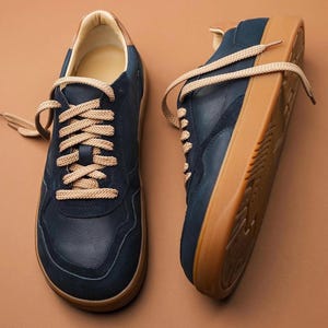 May include: A pair of navy blue sneakers with tan laces and a tan sole. The sneakers have a suede-like texture on the upper and a leather-like trim around the ankle. The laces are thick and round.