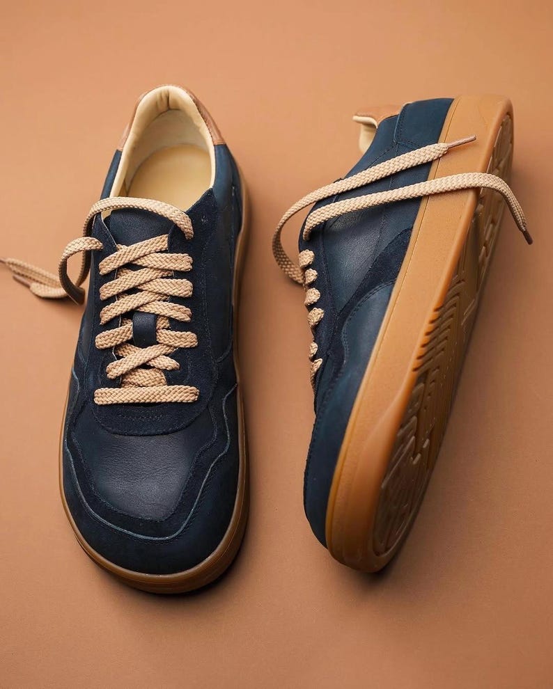 May include: A pair of navy blue sneakers with tan laces and a tan sole. The sneakers have a suede-like texture on the upper and a leather-like trim around the ankle. The laces are thick and round.