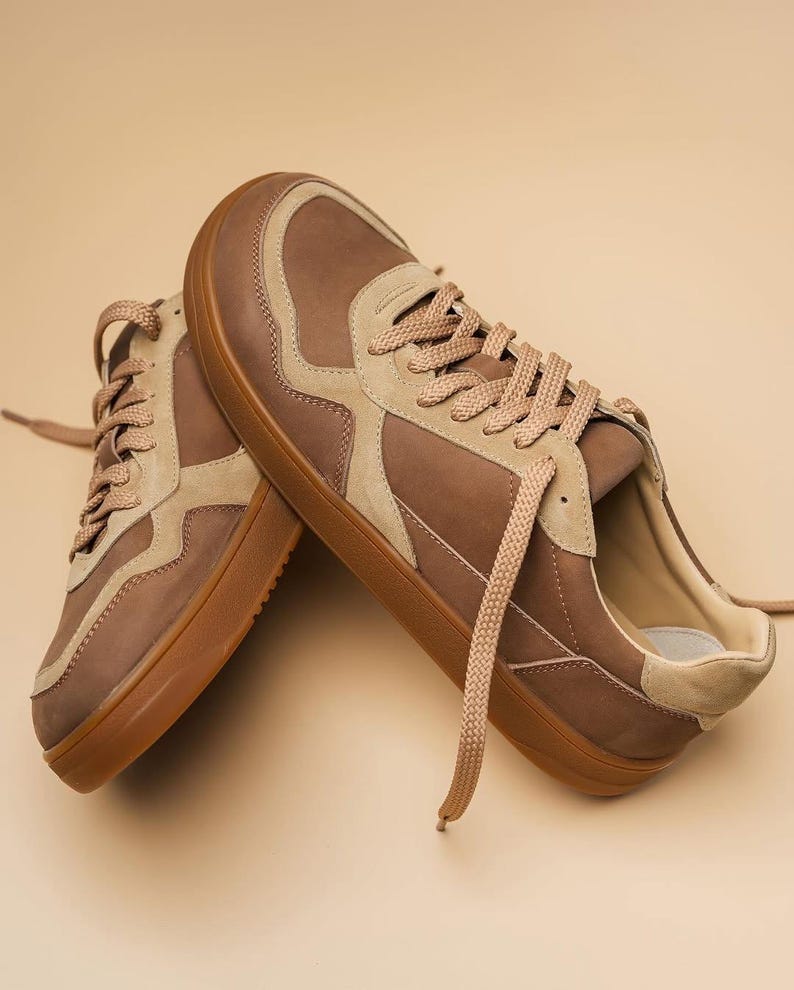 May include: A pair of brown and tan sneakers with matching laces. The shoes have a low-profile design with a rounded toe and a rubber sole. The sneakers are made of leather and suede materials.