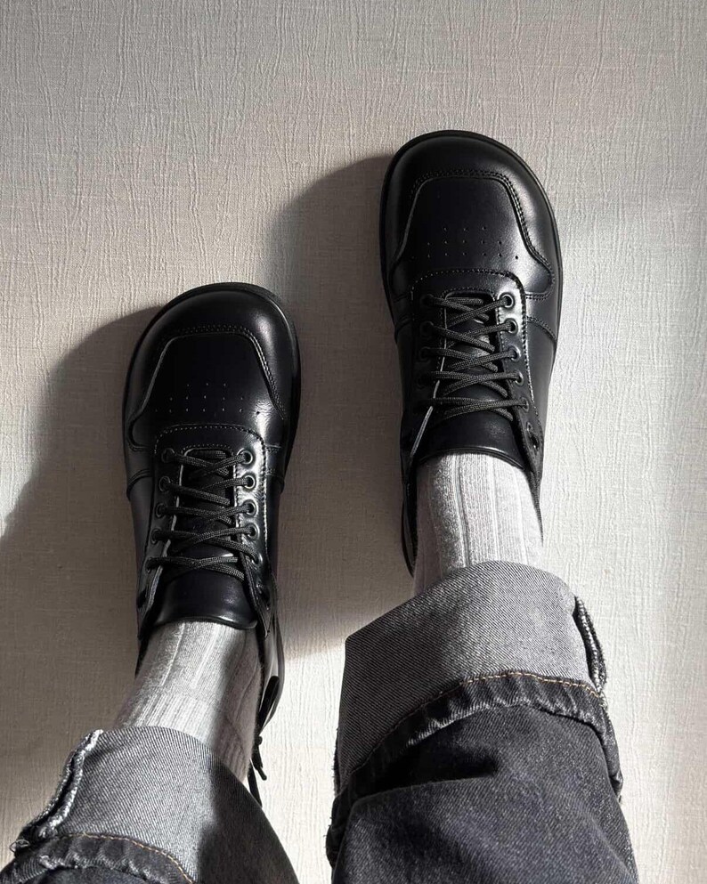 May include: A pair of black leather sneakers with laces, worn with gray socks and denim jeans. The sneakers have a classic design with a rounded toe and a low profile. The jeans are cuffed at the ankles.