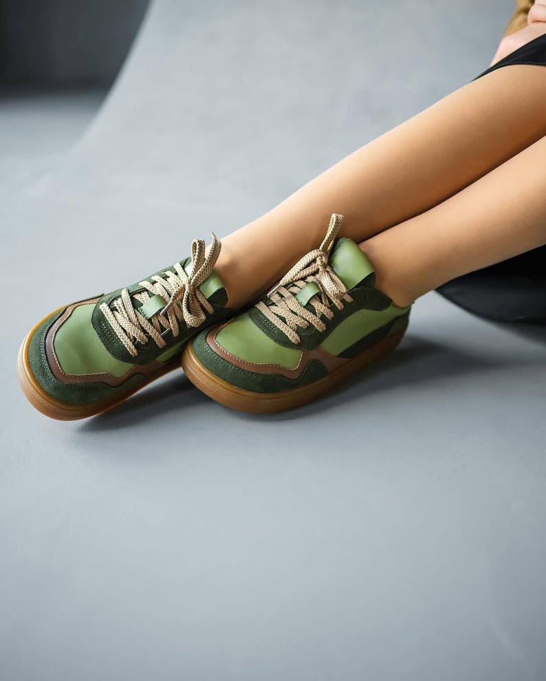May include: Green and brown sneakers with tan laces. The shoes have a rounded toe and a brown sole. The sneakers are made of a combination of materials, including suede and leather. The shoes are designed for casual wear.