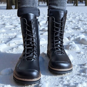 Könnte beinhalten: Ein Paar schwarze, wadenhohe Schnürstiefel mit glatter Oberfläche, abgerundeten Zehenkappen und seitlichem Reißverschluss. Die Stiefel haben eine dicke, dunkle Sohle mit einem hellen Rahmen-Detail und schwarze Schnürsenkel in den Ösen.