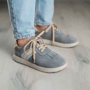 May include: Gray suede sneakers with white soles and light blue and beige accents. The laces are tied in a bow.