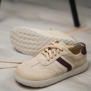 May include: A pair of beige suede sneakers with a brown stripe and white laces. The sneakers have a white rubber sole.