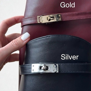 May include: A burgundy leather item with a gold metal buckle and a black leather item with a silver metal buckle. The text Gold, Silver, and Please specify: Gold or Silver metal buckle? are visible on the image, indicating hardware options.
