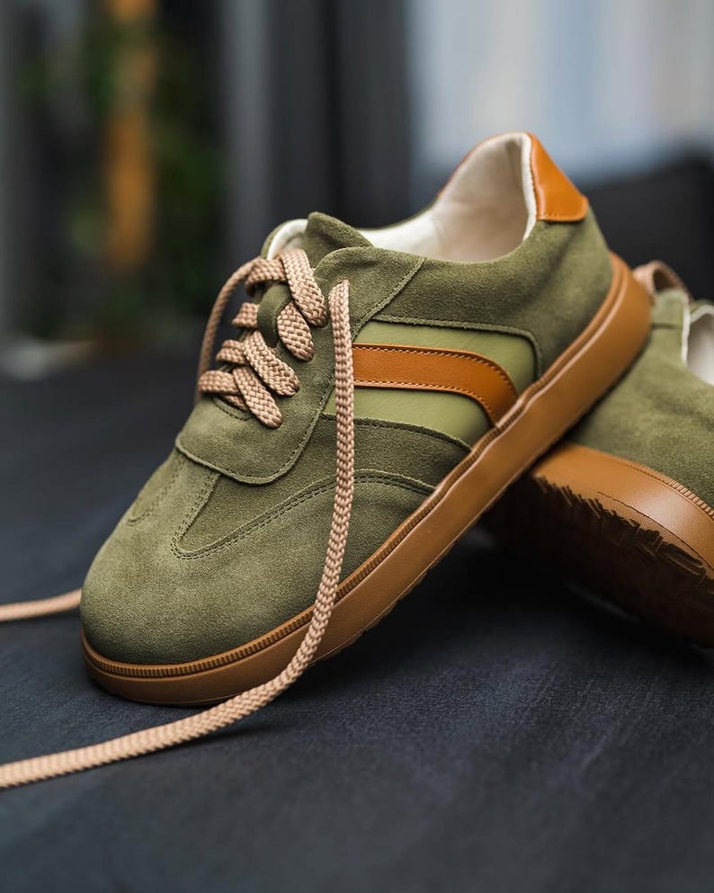 May include: Green suede sneakers with brown and white stripes and brown laces. The sneakers have a brown rubber sole.