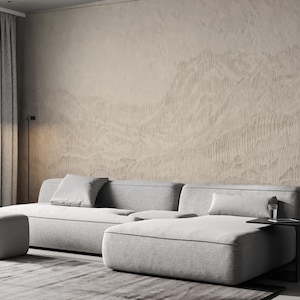 May include: A modern living room featuring a light gray sectional sofa with a matching ottoman. The room has a neutral color palette, with a textured beige wall and gray curtains. A small side table holds a glass.