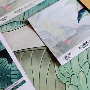 Może przedstawiać: Zbliżenie na próbki tkanin z botanicznym wzorem. Próbki przedstawiają duże zielone liście i kwiatowe wzory w odcieniach zieleni, bieli i różu. Na etykietach widoczny jest napis "LUXURY textile".