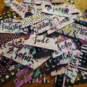 May include: A collection of assorted paper Bible index tabs featuring various floral patterns, black and white stripes, and polka dots. Each tab is printed with the name of a book of the Bible in black script, including Genesis, Psalms, Exodus, Jude, and John.
