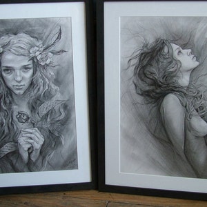 May include: Two framed black and white pencil drawings of women. The drawing on the left shows a woman with long hair and a floral crown holding a flower. The drawing on the right shows a woman with long hair looking up.