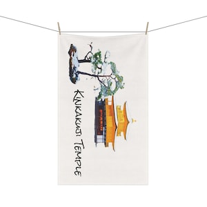 May include: A white towel with a watercolor illustration of a golden temple with a snow-covered pine tree in front of it. The text "Kinkakuji Temple" is written vertically on the left side of the image.