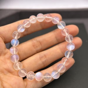 May include: A white moonstone bracelet with iridescent shimmer. The bracelet is made of round beads and is strung on a clear elastic cord.