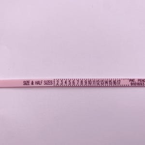 May include: Pink plastic ring sizer with a black arrow and the text "SIZE & HALF SIZES 1 2 3 4 5 6 7 8 9 10 11 12 13 14 15 16 17" and "PAT. PEND. 9101693".