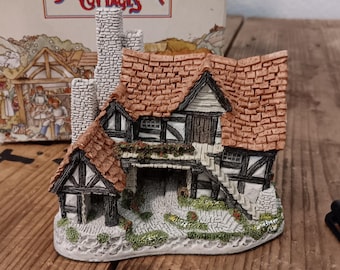 May include: A miniature cottage figurine with a red-tiled roof, stone chimney, and black and white timber framing. The figurine is part of the "David Winter Cottages" collection, with the box visible in the background. The cottage sits on a wooden surface.